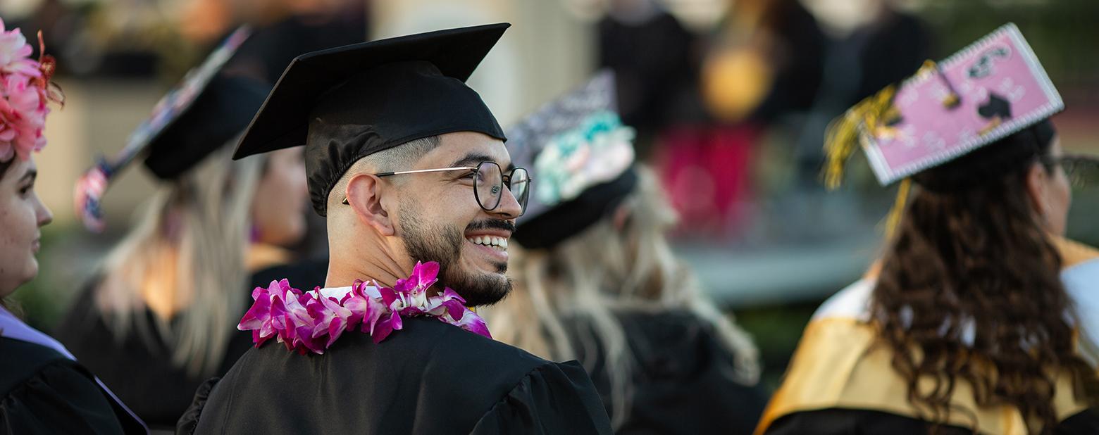 照片中，一名E世博ESBALL的毕业生戴着学士帽，穿着学士服，望着乌鸦. 